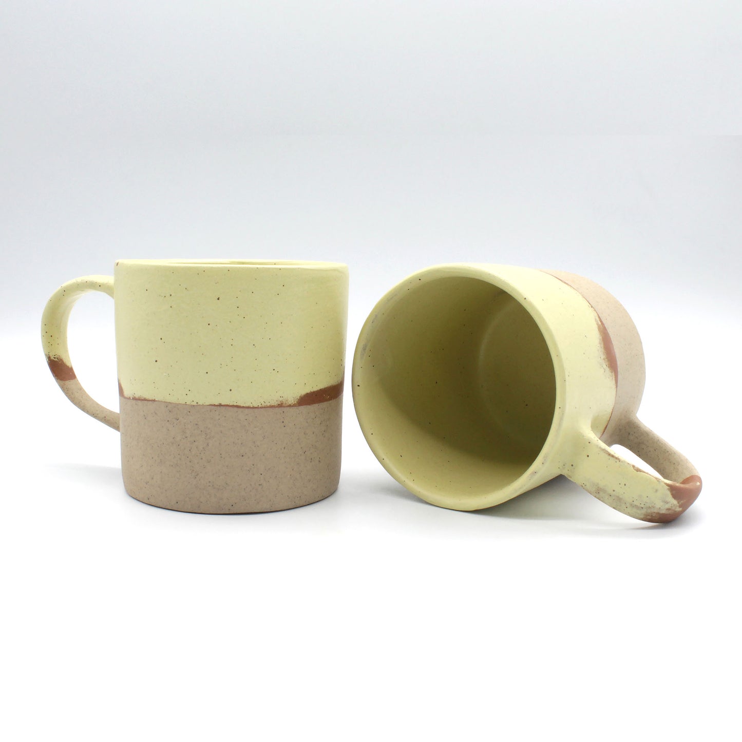 Two handmade Daorueng mugs, one mug upright, and one lying on its side to show the parmesan yellow interior.