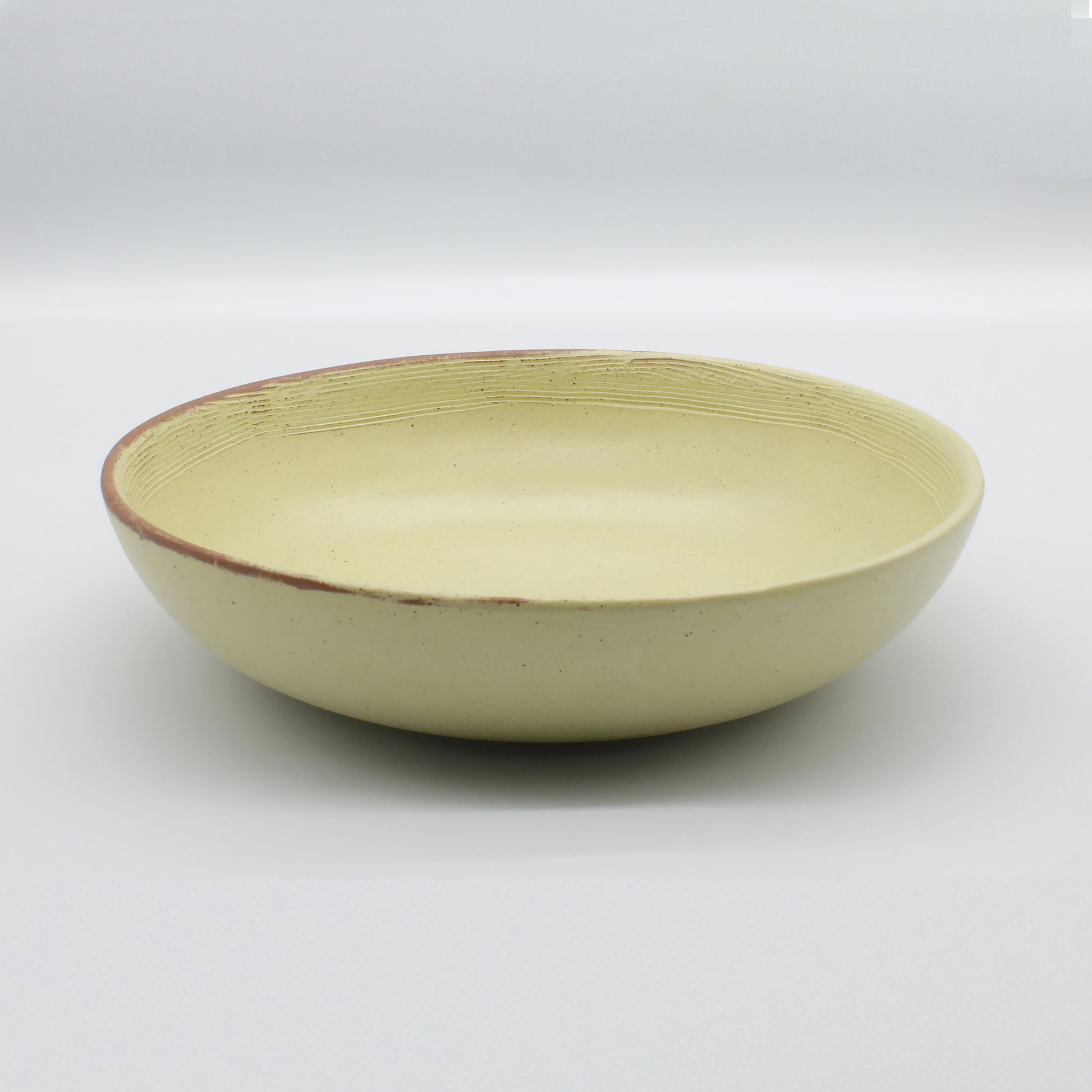 Side on view of beautiful handmade pasta bowl from Thailand, yellow and natural clay speckled rustic