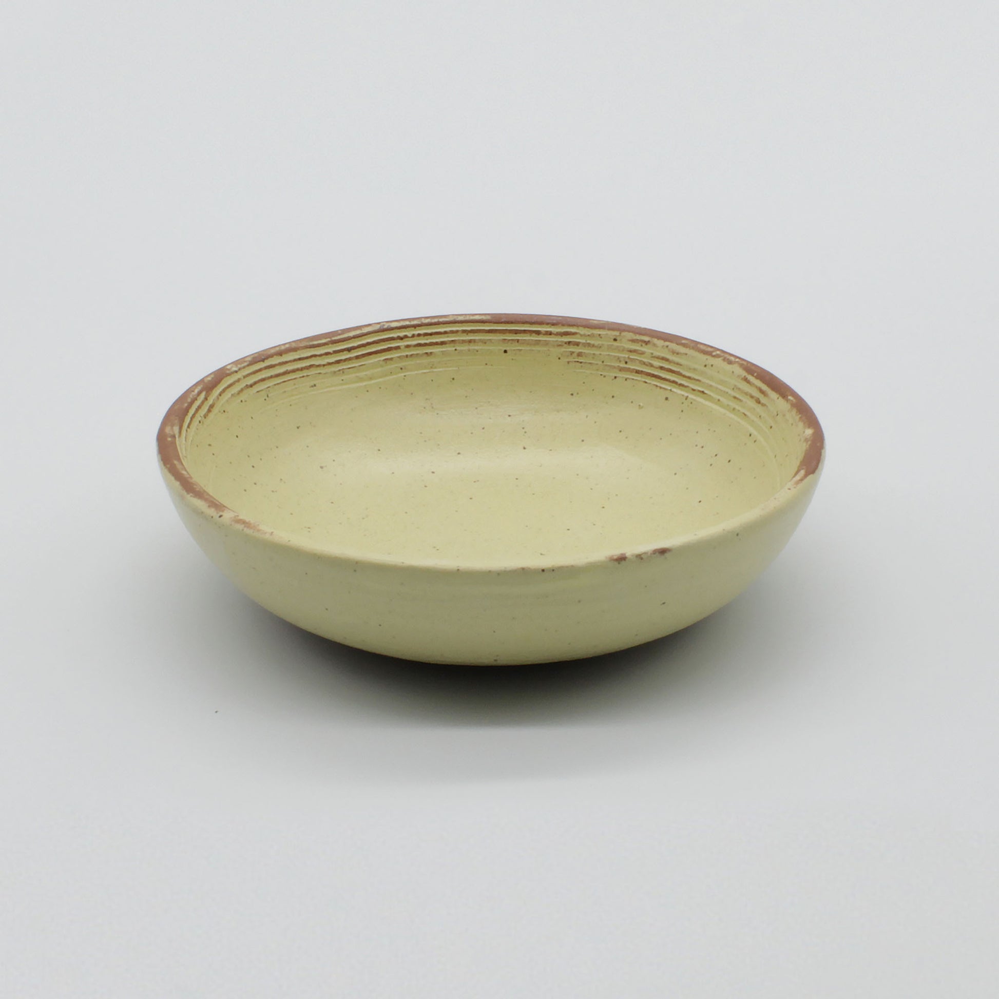 Side view of handmade ceramic sauce bowl from Thailand, yellow and natural speckled clay rustic