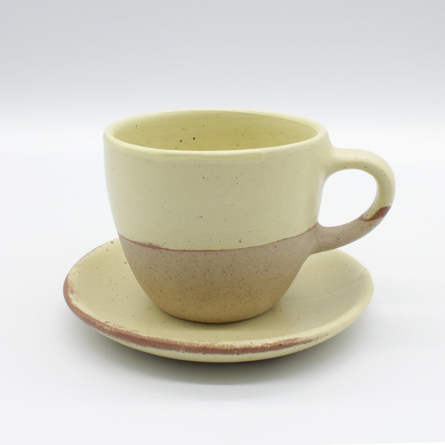 Beautiful handmade ceramic tea cup and saucer. Yellow and natural clay speckled on a white background