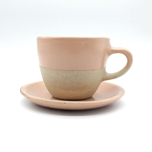 Side on view of beautiful handmade ceramic tea set from Thailand. Cup and saucer with pink, peach colour at the top and natural clay at the bottom. Unique, natural rustic look